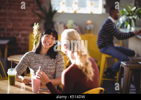 Freundliche weibliche Freunde sprechen während der Sitzung mit frischen Getränken am Tisch im Café Stockfoto