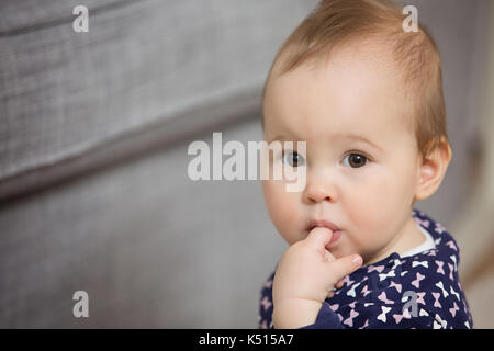 Neun Monate altes Baby Mädchen ihren Finger in den Mund stecken den Schmerz der das Zahnen zu erleichtern, mit offenen Augen Stockfoto