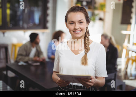 Portrait von lächelnden jungen Kellnerin mit Menü im Cafe Stockfoto