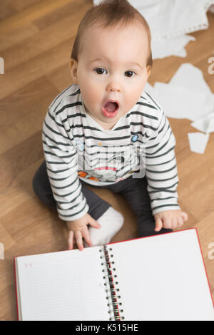 Zehn Monate altes Baby Mädchen spielen mit Papieren und Papier Ordner auf dem Fußboden; Abreißen des Papiers und die Schaffung eines Chaos im Zimmer Stockfoto