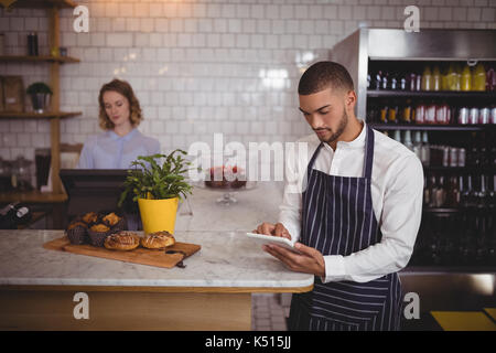 Junger Kellner mit digitalen Tablet im Stehen durch Zähler in Coffee Shop Stockfoto