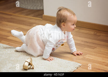 Ein Jahr alten Baby Mädchen in weißem Hemd und satin Kleid kriechen auf dem Boden gekleidet Stockfoto