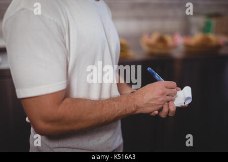 Mittelteil der Kellner schreiben auf Notepad bei Coffee Shop Stockfoto