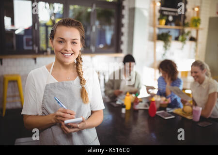 Portrait von lächelnden jungen Kellnerin mit Notepad stehen im Cafe Stockfoto