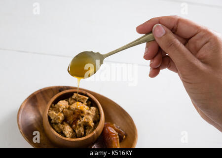 Nahaufnahme der womans Hand gießen Honig in Cornflakes Schale Stockfoto
