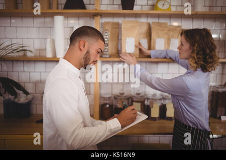 Seitenansicht des jungen männlichen Besitzer schreiben auf Zwischenablage während Kellnerin Vermittlung von Produkten bei Coffee Shop Stockfoto