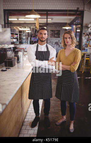 Portrait von selbstbewussten jungen Kellner mit Waffen durch Zähler in Coffee Shop gekreuzt Stockfoto