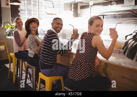 Portrait von lächelnden jungen Freunde halten Getränke beim Sitzen an der Theke im Café Stockfoto