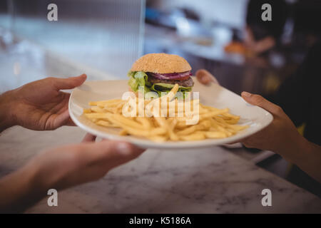 7/8 Hände der Kellner und Köchin halten frische Burger und Pommes frites Platte an der Theke im Café Stockfoto