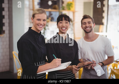 Portrait von fröhlicher junger Mitarbeiter warten Holding digital Tablet mit Notepad und Zwischenablage an Coffee Shop Stockfoto