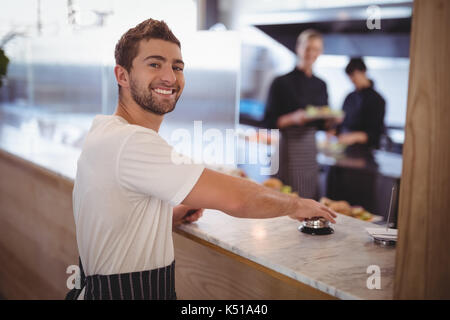 Portrait von lächelnden Kellner Drücken der Klingel Zähler bei Coffee Shop Stockfoto