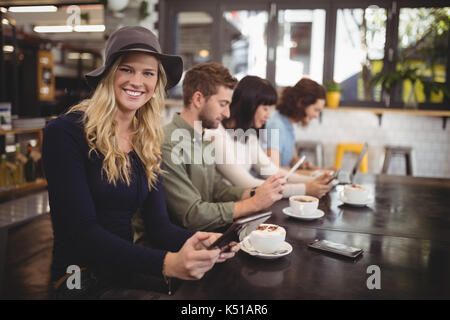 Portrait von lächelnden jungen Frau sitzt mit Freunden am Tisch im Cafe Stockfoto