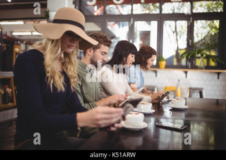 Junge Freunde mit Handys beim Sitzen mit Kaffeetassen bei Tisch im Cafe Stockfoto