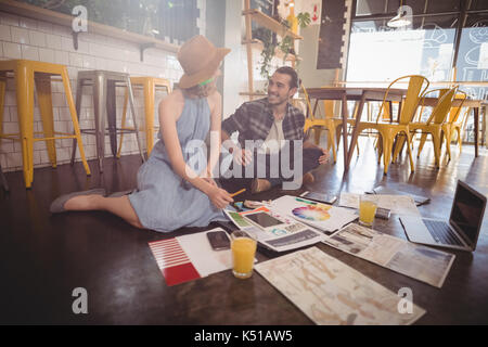 Smiling Young Professionals mit Blätter und Technologien auf dem Boden im Coffee Shop Stockfoto