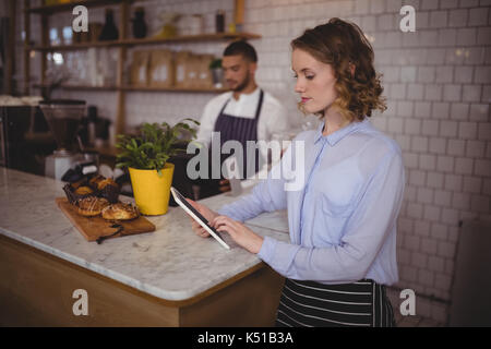 Junge Kellnerin mit Tablet Computer, während an der Theke im Café stehend Stockfoto