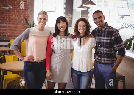 Portrait von lächelnden jungen Freunde stehend mit Arme um im Coffee Shop Stockfoto