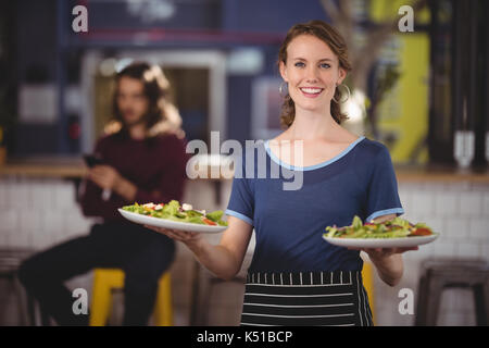 Portrait von lächelnden jungen Kellnerin mit frischem Salat Teller zum Coffee Shop Stockfoto