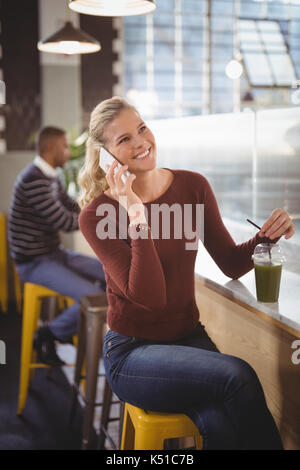 Gerne schöne blonde Frau im Gespräch über celllphone beim Sitzen an der Theke mit Getränk im Café Stockfoto