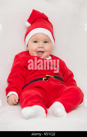 Sieben Monate alten Baby Mädchen in Santa Claus Kleid sitzt auf einer weißen Decke Stockfoto