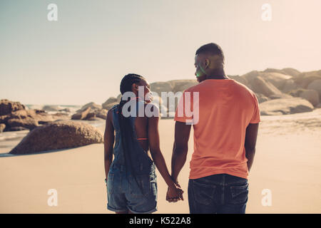 Afrikanische amerikanische Paar Hände halten und zu Fuß am Strand entlang. Mann und Frau in der Liebe ein Spaziergang an der Küste im Sommer Stockfoto