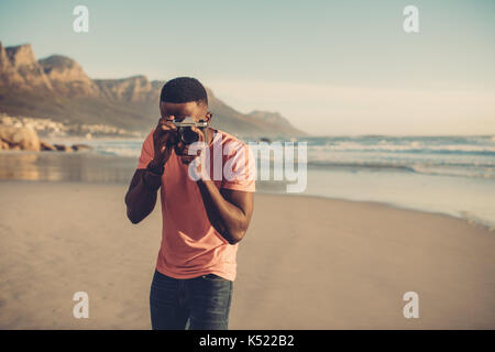 Afrikanischer Mann die Bilder mit digitalen Kamera am Strand. Junger Mann nimmt an der Küste. Stockfoto