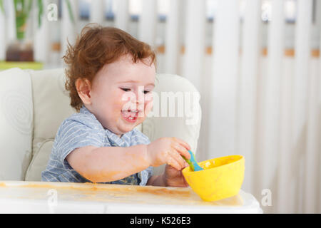 Cute baby boy Essen selbst auf hoher Stuhl Stockfoto