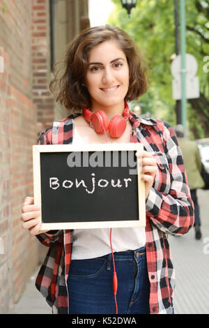 Junge schöne Frau mit Schiefertafel mit Text "Bonjour". Im Freien. Stockfoto