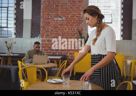 Junge Kellnerin Gläser mit Geschäftsmann mit Laptop am Tisch im Cafe Stockfoto