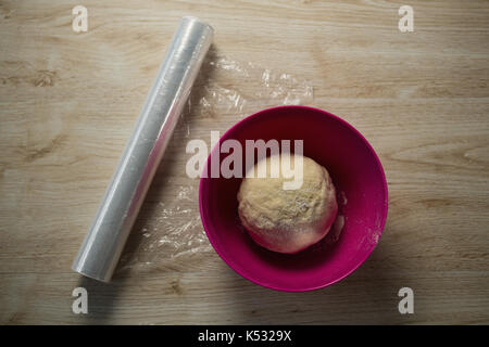 Ansicht von oben Der Knetete Teig in rosa Schale auf der Plastikfolie am Tisch Stockfoto