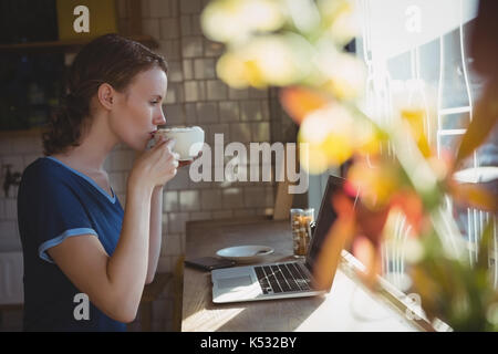 Junge Frau mit Laptop Kaffee trinken an der Fensterbank im Cafe Stockfoto