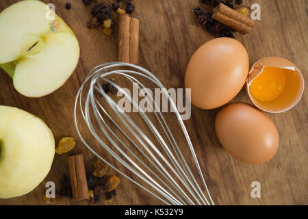Nahaufnahme von Kabel schneebesen von Eiern mit Gewürzen und Granny Smith Apfel auf hölzernen Tisch Stockfoto