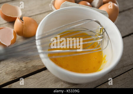 In der Nähe von Egg in der Schüssel mit Draht schneebesen von Eierschalen auf hölzernen Tisch Stockfoto