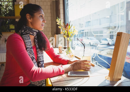 Nachdenkliche junge Frau mit Getränk an der Fensterbank im Cafe sitzen Stockfoto