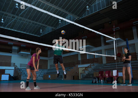 Volle Länge des männlichen Volleyballer mit Mannschaftskameraden am Hof springen Stockfoto