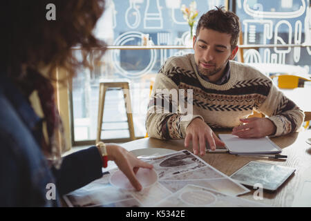 Junger Mann mit Frau diskutieren über Diagramm am Tisch im Cafe Stockfoto