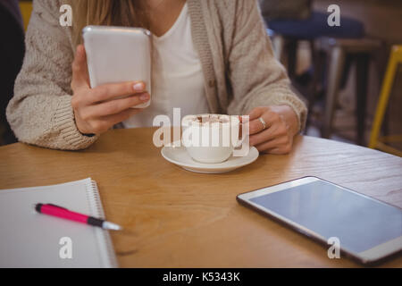 Den mittleren Abschnitt der Frau mit Kaffee mit Phone am Tisch im Cafe Stockfoto