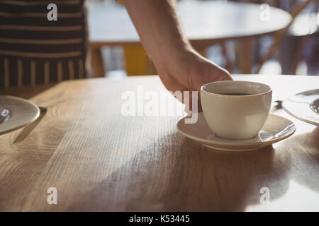 7/8 Hand der Kellner serviert Kaffee auf hölzernen Tisch im Cafe Stockfoto