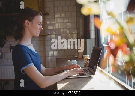 Seitenansicht des junge Frau mit Laptop an der Fensterbank im Cafe Stockfoto