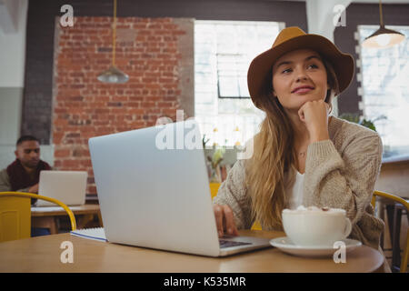 Nachdenkliche junge Frau mit Laptop weg schauen im Cafe Stockfoto