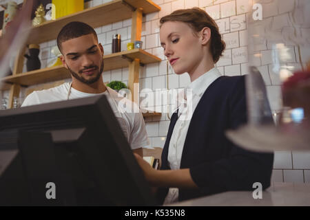 Besitzerin mit jungen Kellner mit Kasse beim Stehen in der Cafe Stockfoto