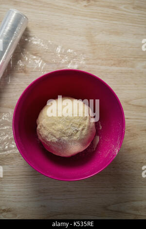 Draufsicht des Teigs in rosa Schale auf der Plastikfolie am Tisch Stockfoto