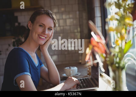 Portrait von lächelnden jungen Frau mit Laptop an der Fensterbank im Cafe Stockfoto