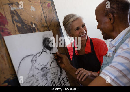Lächelnd senior Frau Unterstützung der Mann beim Malen auf Papier in der Kunst Klasse Stockfoto