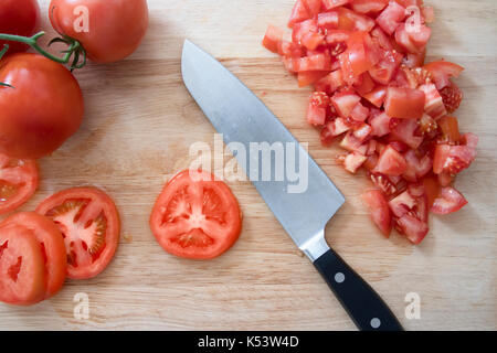 Tomaten/Paradeiser, ganz, in Scheiben geschnitten, gehackt, auf Schneidebrett mit Messer. Stockfoto