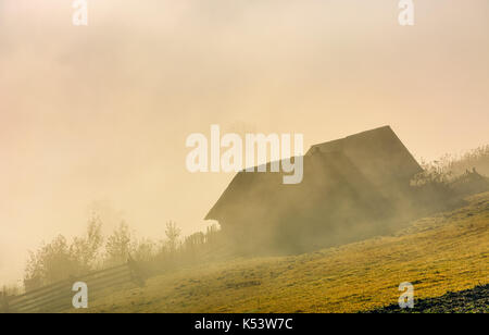 Wunderschöne herbstliche Landschaft Landschaft verlassene Scheune am Hang in kranken Nebel bei Sonnenaufgang Stockfoto