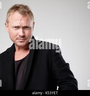 Ein junger Mann mit zerzausten Haar und schwarze Kleidung, schaut die Kamera in Unmut. Stockfoto