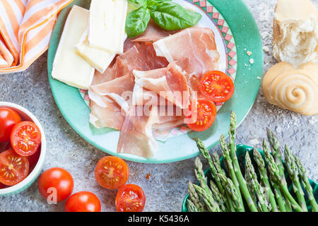 Köstliche Speisen der Italienischen crudo Schinken, frische grüne Spargelspitzen, Brie Käse und Tomaten mit einem frisch gebackenen Brötchen serviert. Stockfoto