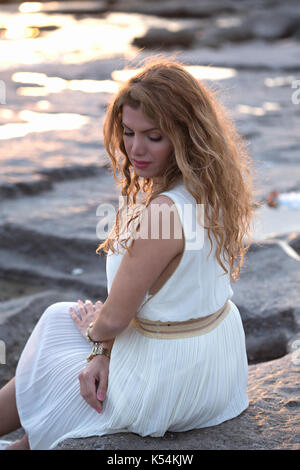 Schöne Dame in Elfenbein Kleid sitzen auf den Felsen und Denken Stockfoto