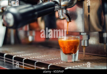 Glas frischen Espresso mit einer fallenden Tropfen auf. Der Prozess, in dem Kaffee auf eine Kaffeemaschine in einem Café. Stockfoto