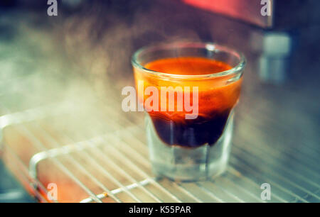 Nahaufnahme eines Glas mit frisch gebrühten Espresso auf eine Kaffeemaschine in einem Dampf. Stockfoto